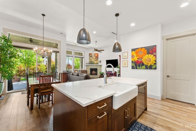 kitchen featuring a sink, a fireplace, light wood-style floors, dishwasher, and ceiling fan with notable chandelier