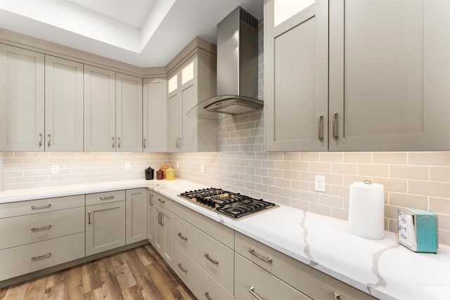 kitchen featuring decorative backsplash, light stone countertops, light wood-style floors, wall chimney range hood, and stainless steel gas stovetop