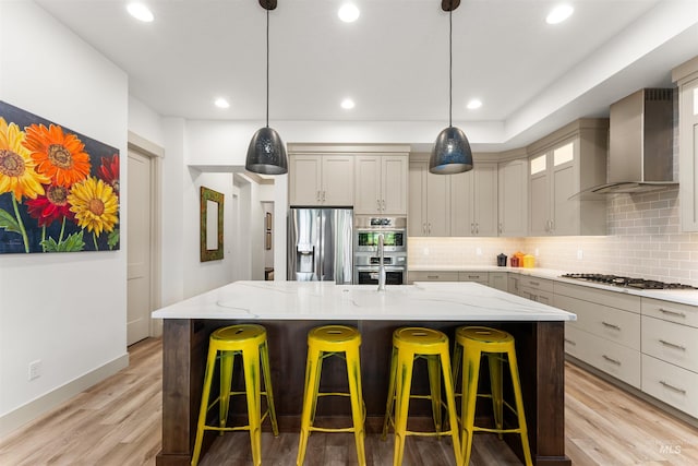 kitchen with light stone countertops, wall chimney exhaust hood, light wood-style flooring, backsplash, and stainless steel appliances