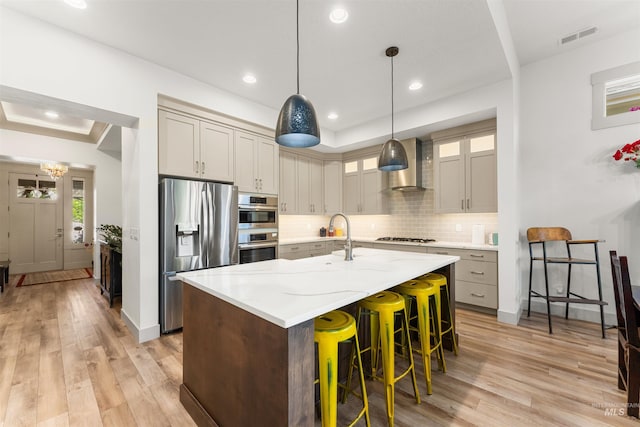 kitchen featuring wall chimney range hood, stainless steel appliances, light wood finished floors, and visible vents