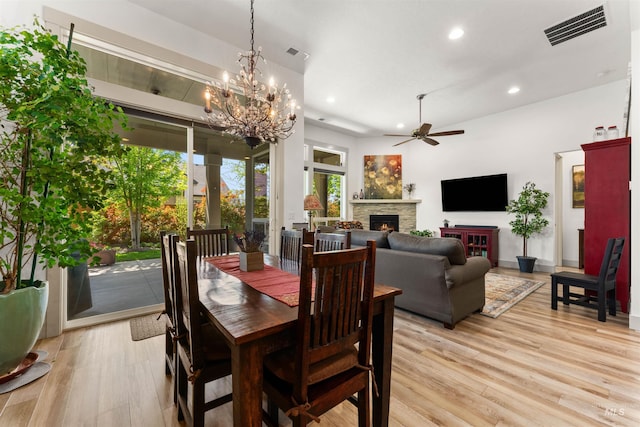 dining room with visible vents, a stone fireplace, recessed lighting, light wood-type flooring, and ceiling fan with notable chandelier