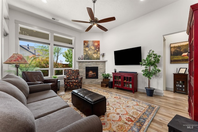 living area with ceiling fan, a stone fireplace, baseboards, wood finished floors, and visible vents