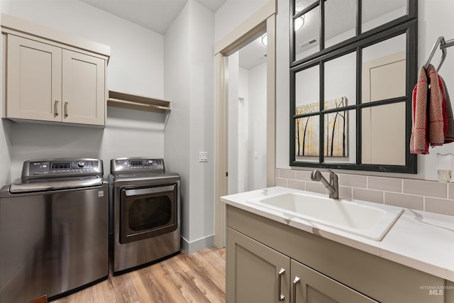 laundry room featuring cabinet space, a sink, baseboards, light wood-style floors, and washer and clothes dryer