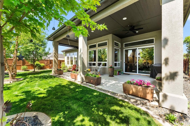 exterior space with fence, stucco siding, a lawn, a ceiling fan, and a patio