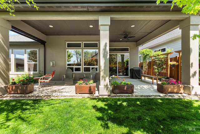 back of property with a ceiling fan, stucco siding, a yard, and a patio area