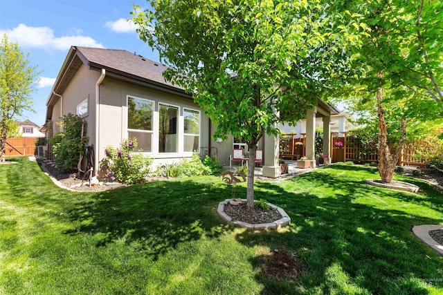 rear view of property featuring stucco siding, fence, and a yard