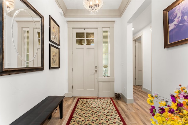entryway with baseboards, ornamental molding, light wood-style flooring, and a chandelier