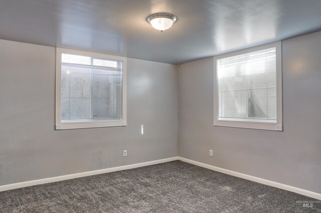 empty room featuring dark colored carpet, plenty of natural light, and baseboards