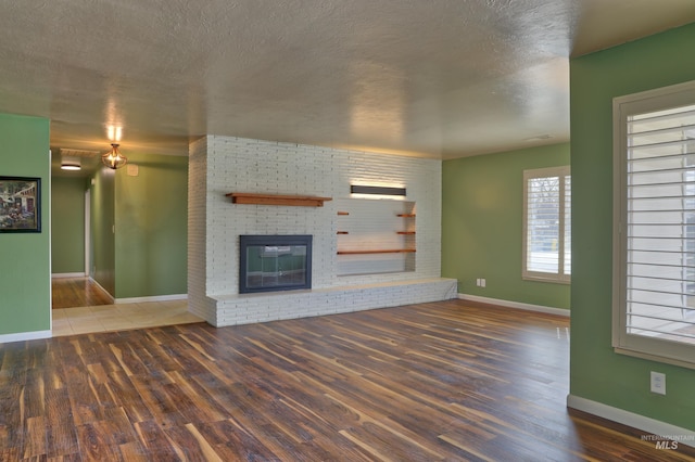 unfurnished living room featuring a fireplace, a textured ceiling, wood finished floors, and baseboards