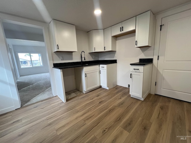 kitchen with a sink, light wood-type flooring, dark countertops, and white cabinetry