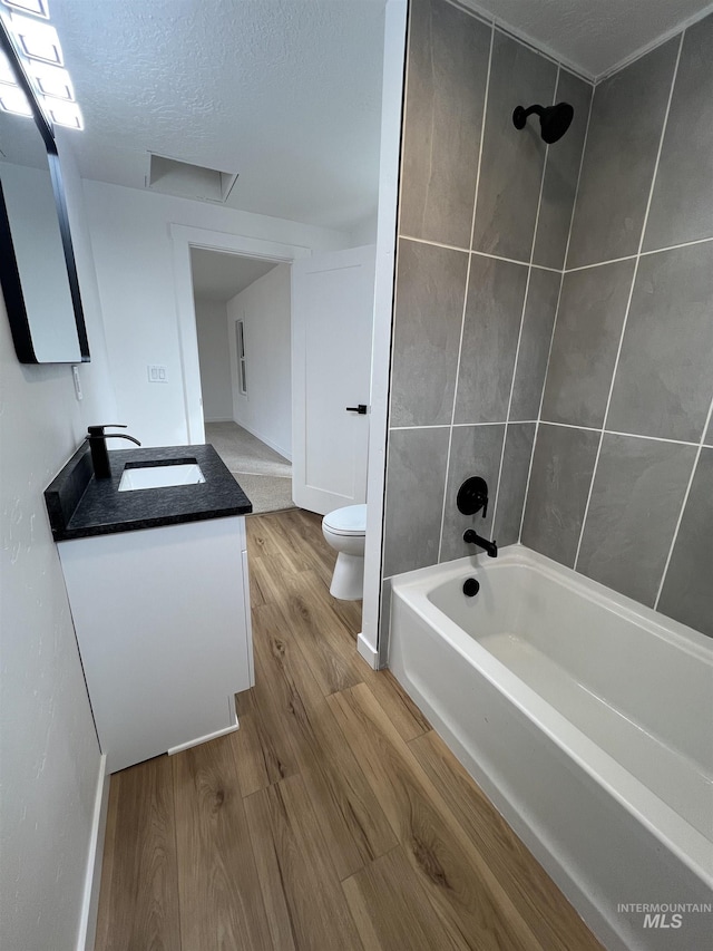 bathroom with toilet, a textured ceiling, wood finished floors, tub / shower combination, and vanity