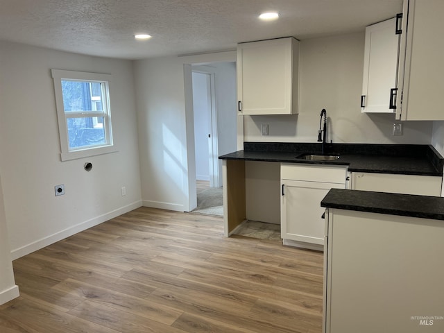 kitchen featuring baseboards, a sink, white cabinets, light wood-style floors, and a textured ceiling