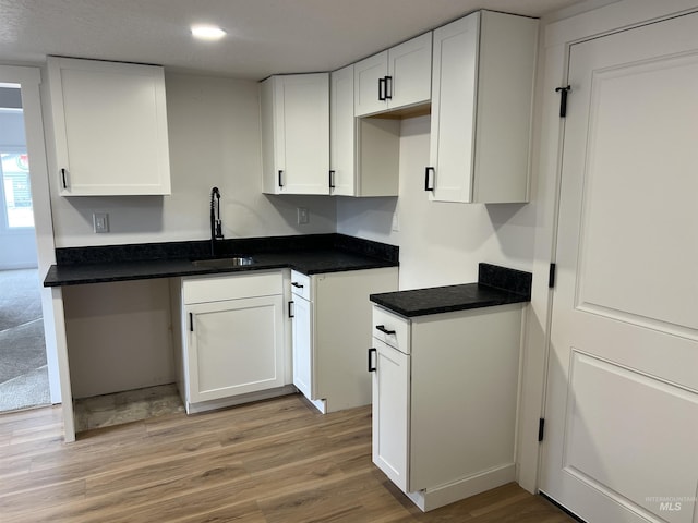 kitchen featuring white cabinetry, dark countertops, light wood-style flooring, and a sink