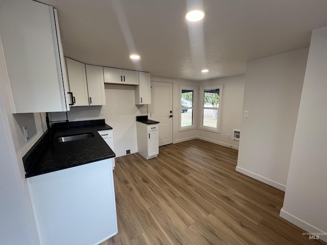 kitchen featuring dark countertops, baseboards, light wood-style floors, white cabinets, and a sink