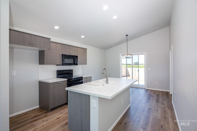 kitchen with vaulted ceiling, an island with sink, black appliances, light hardwood / wood-style flooring, and sink