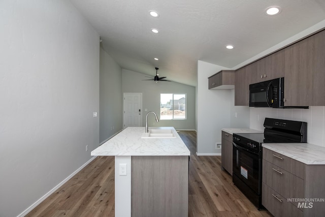 kitchen featuring vaulted ceiling, black appliances, ceiling fan, hardwood / wood-style flooring, and a kitchen island with sink