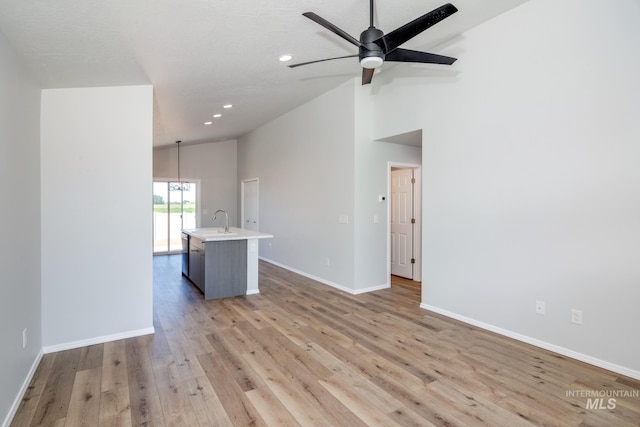 unfurnished living room with light wood-type flooring, a textured ceiling, sink, high vaulted ceiling, and ceiling fan