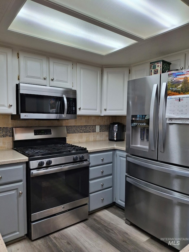 kitchen with stainless steel appliances, gray cabinetry, wood finished floors, and tasteful backsplash