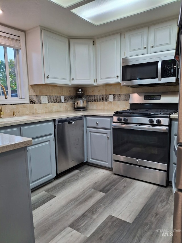 kitchen with appliances with stainless steel finishes, light wood finished floors, decorative backsplash, white cabinetry, and light countertops