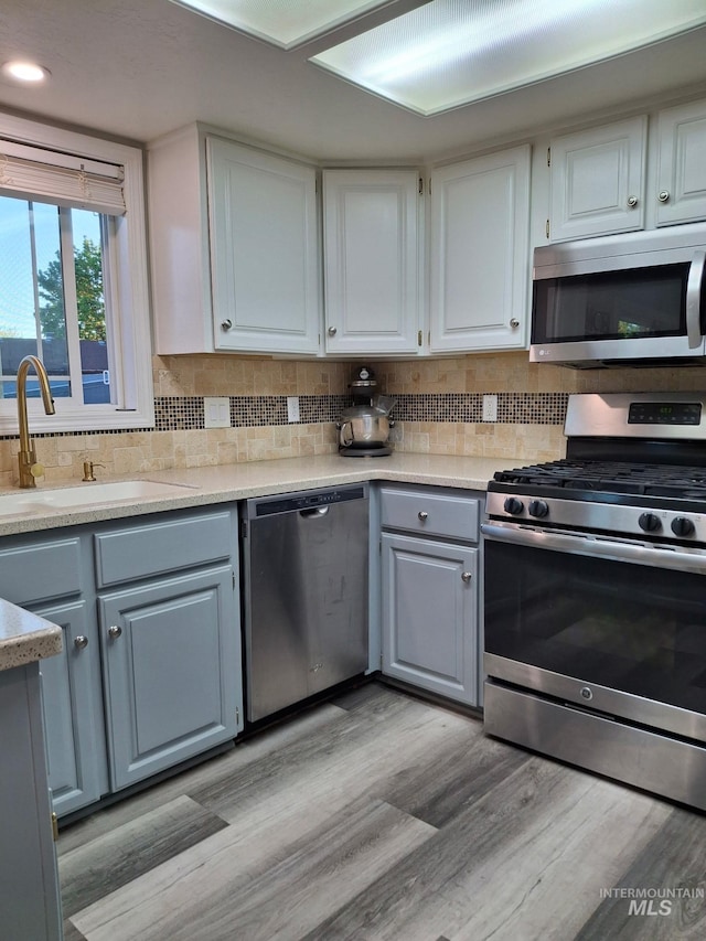 kitchen featuring stainless steel appliances, a sink, decorative backsplash, light countertops, and white cabinetry
