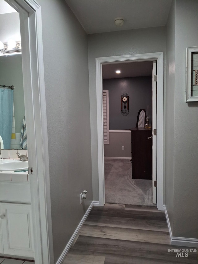 hallway featuring wood finished floors, a sink, and baseboards