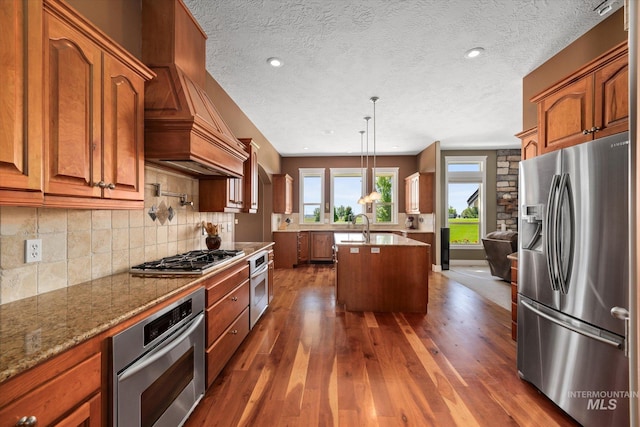 8585 W Rioja St, Star, ID 83669 - kitchen with appliances with stainless steel finishes, custom range hood, a center island with sink, dark wood-type flooring, and a textured ceiling