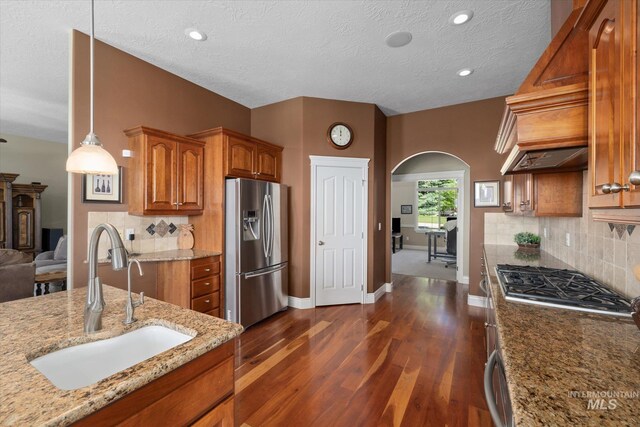 8585 W Rioja St, Star, ID 83669 - kitchen featuring stainless steel appliances, a sink, arched walkways, brown cabinetry, and dark wood-type flooring