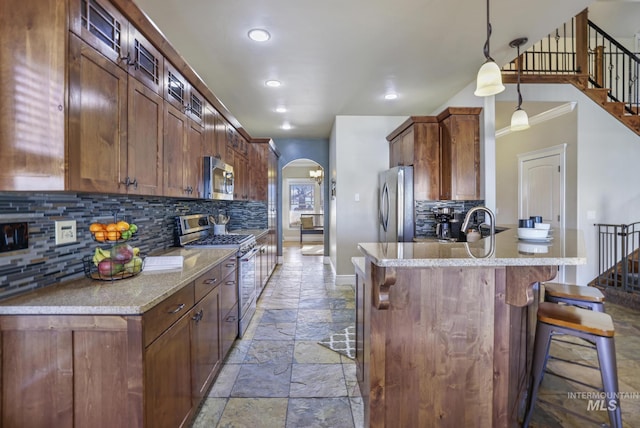 kitchen with light stone counters, hanging light fixtures, stainless steel appliances, tasteful backsplash, and a kitchen bar