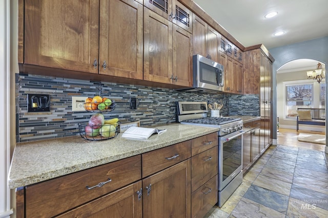 kitchen with light stone counters, a chandelier, stainless steel appliances, backsplash, and crown molding