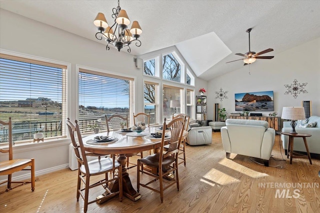 dining area featuring high vaulted ceiling, ceiling fan with notable chandelier, a textured ceiling, light wood finished floors, and baseboards