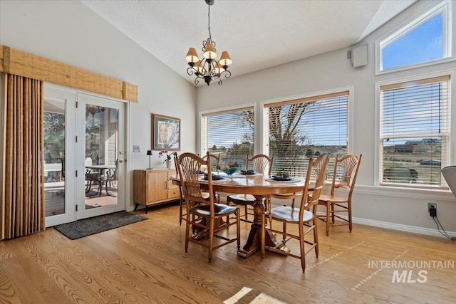 dining room featuring light wood-type flooring, a textured ceiling, baseboards, a chandelier, and vaulted ceiling