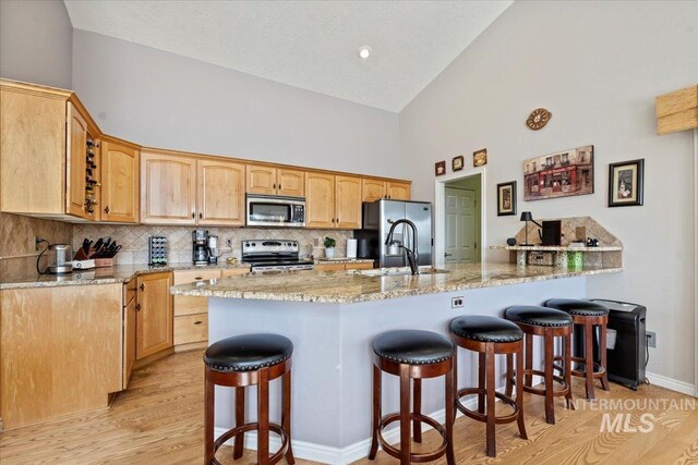 kitchen featuring light stone countertops, a kitchen bar, appliances with stainless steel finishes, a peninsula, and a sink