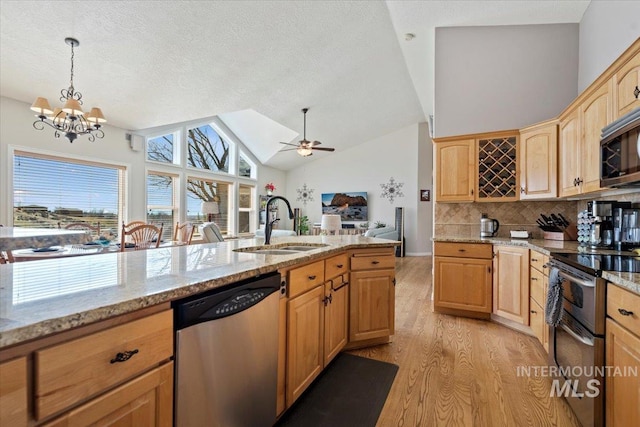 kitchen with light brown cabinetry, vaulted ceiling, light wood-style floors, stainless steel appliances, and a sink