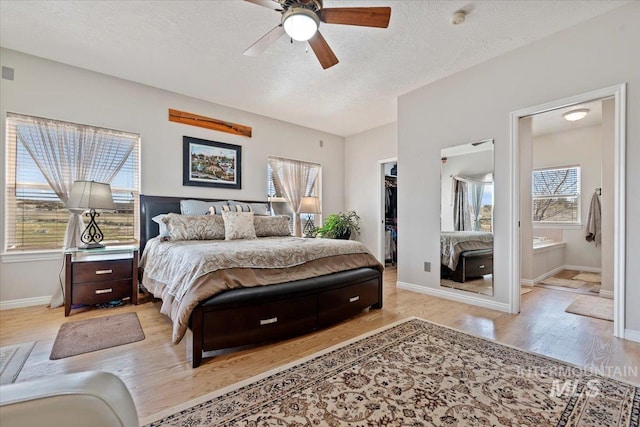 bedroom with wood finished floors, baseboards, ensuite bath, a spacious closet, and a textured ceiling