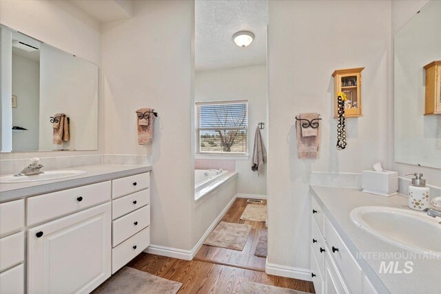 bathroom with a textured ceiling, two vanities, wood finished floors, and a sink