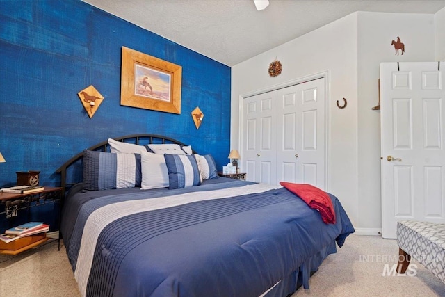 bedroom with a textured ceiling, a closet, carpet, baseboards, and an accent wall