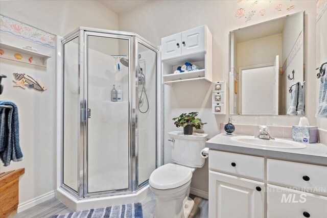 full bath featuring vanity, toilet, baseboards, and a stall shower