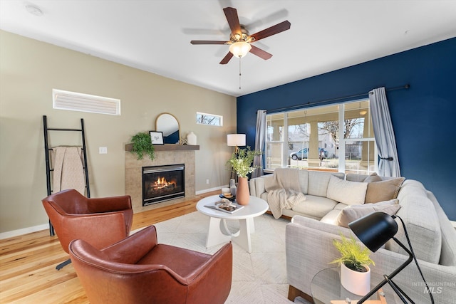 living room featuring a tiled fireplace, ceiling fan, and light hardwood / wood-style flooring