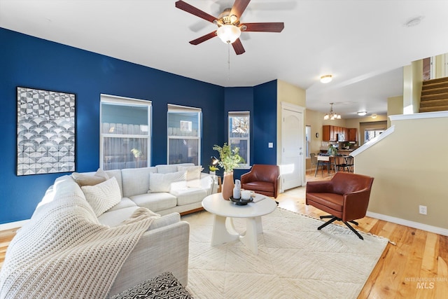 living room with light wood-type flooring and ceiling fan with notable chandelier