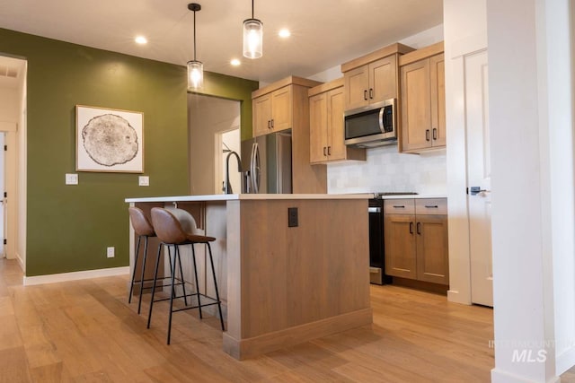 kitchen with tasteful backsplash, a center island with sink, appliances with stainless steel finishes, and light wood-style floors