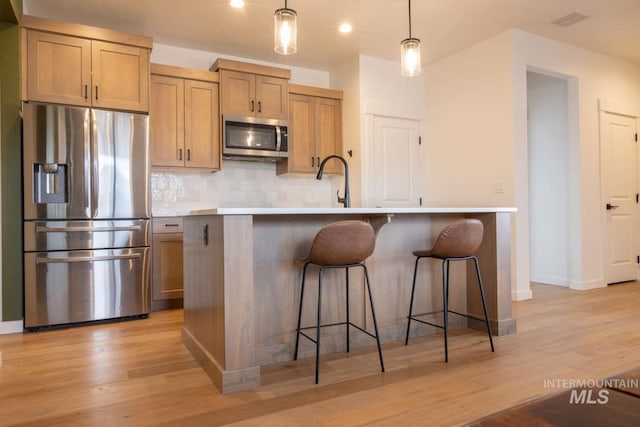 kitchen with an island with sink, backsplash, appliances with stainless steel finishes, and light wood-type flooring