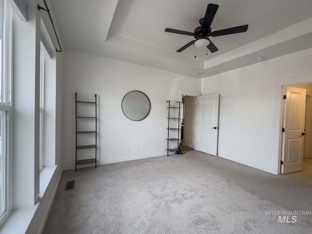 unfurnished bedroom featuring a tray ceiling, carpet flooring, visible vents, and baseboards