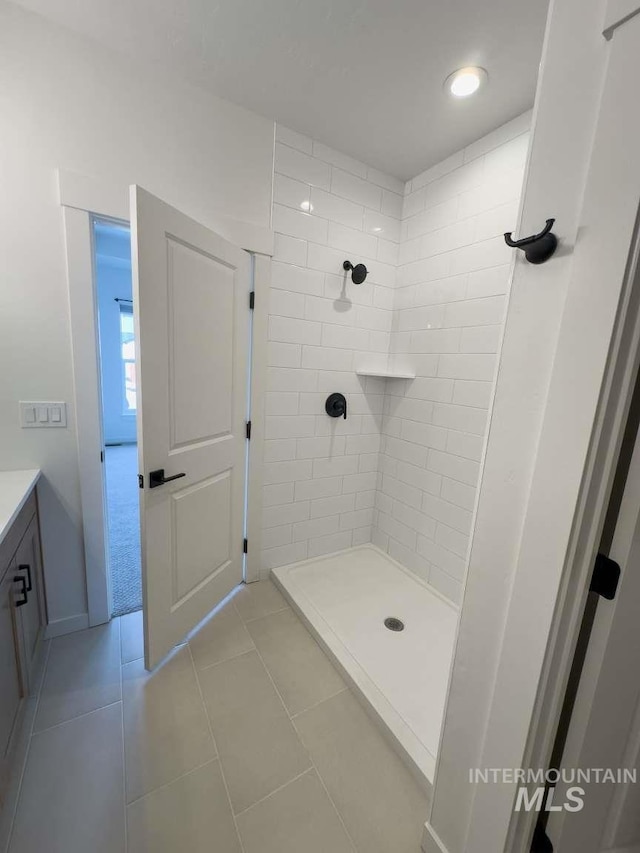 full bath featuring a tile shower, tile patterned flooring, vanity, and baseboards