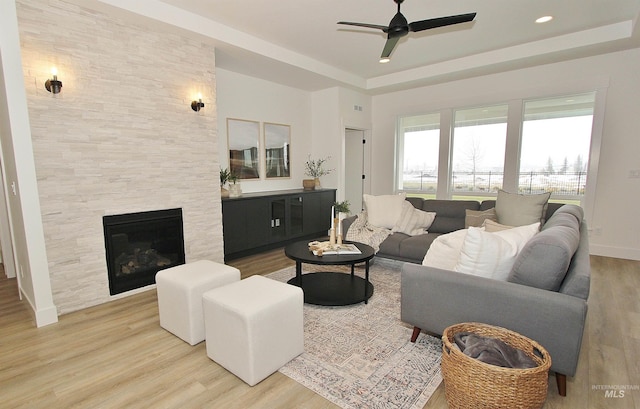 living room with wood-type flooring, a large fireplace, a raised ceiling, and ceiling fan