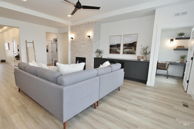 living room featuring light wood-type flooring, ceiling fan, and a fireplace