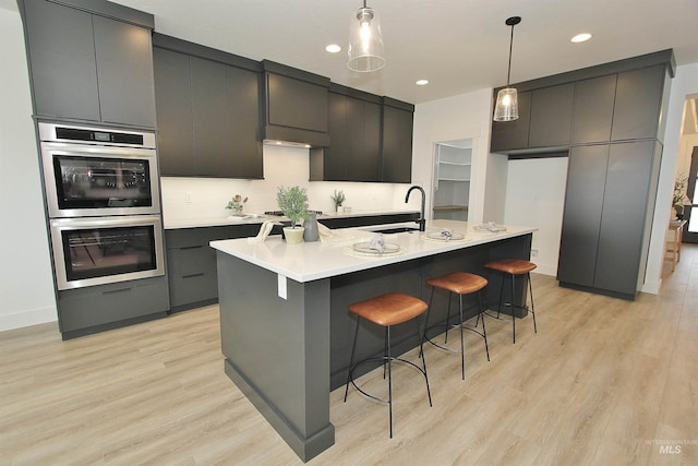 kitchen featuring sink, hanging light fixtures, appliances with stainless steel finishes, and a center island with sink