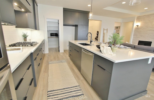 kitchen featuring a center island with sink, stainless steel appliances, gray cabinetry, hanging light fixtures, and sink