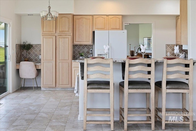 kitchen featuring light brown cabinetry, decorative light fixtures, a breakfast bar area, white fridge with ice dispenser, and light stone countertops