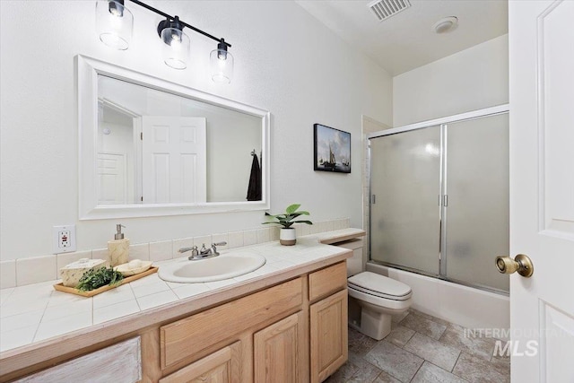 full bathroom featuring bath / shower combo with glass door, vanity, and toilet