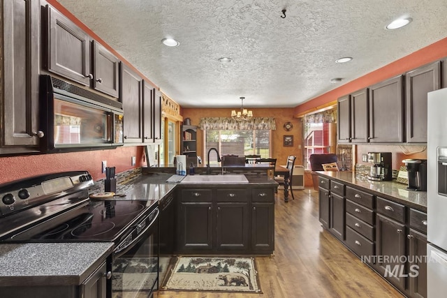 13098 Hillhouse Loop, Donnelly, ID 83615 - kitchen with black appliances, a peninsula, a sink, a chandelier, and light wood-style floors